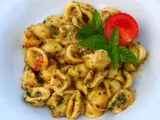 Pyszne makaron orecchiette z sosem pomidorowo-ziołowym, udekorowane listkami bazylii i pomidorem.