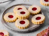 Ein Teller voller **die besten Spitzbuben der Welt**, bestäubt mit Puderzucker, mit leuchtend roter Marmeladenfüllung.