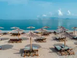 Plaża z leżakami i parasolami, idealna na relaks nad morzem. W oddali widać góry i błękitne niebo.
