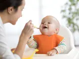 Mama karmi uśmiechniętego niemowlaka łyżeczką. To idealny przykład, co na śniadanie dla niemowlaka – zdrowo i radośnie!