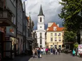 Ulica w jednym z miast na zachodzie Polski, z kościołem w tle i ludźmi spacerującymi po rynku.