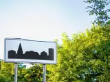 Znak informuje o wjeździe do obszaru zabudowanego. Sylwetka miasta na białym tle.