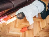 Man in orange gloves cleaning wooden floor with a pink cloth.