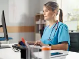 Pielęgniarka w niebieskim uniformie pracuje przy komputerze. Jej specjalizacja pielęgniarska to 5 lat doświadczenia.