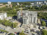 Budowa bloku mieszkalnego w Kołobrzegu. Widok z lotu ptaka na plac budowy, dźwig, samochody i okoliczne budynki. Ceny mieszkań Kołobrzeg mogą być różne.