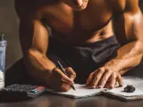 Un athlète calcule combien de protéine par jour il doit consommer, avec un shaker de poudre, une calculatrice et un carnet.