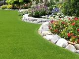 Magnifique pelouse verte bordée de fleurs colorées et d'une murette en pierres, parfaite pour faire bordure jardin.
