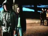 Donnie Darko w bluzie z kapturem i koszulce z nadrukiem szkieletu, obok dziewczyny. W tle dwie postacie w kostiumach.