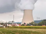 Dampf steigt aus einem Kühlturm eines Atomkraftwerks auf, daneben ein Dorf und ein Maisfeld.
