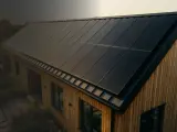 Nowoczesny dom z drewnianą elewacją i panele fotowoltaiczne na dachu. To wizualizacja produkcji energii z fotowoltaiki w poszczególnych miesiącach.