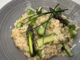 Kremowe risotto z zielonymi szparagami i szczypiorkiem na szarym talerzu.