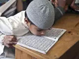 Chłopiec w czapce na głowie pochyla się nad Kor'anem, ucząc się o senegalskiej religii.