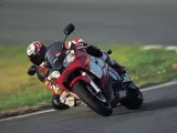 Motocyklista na torze pochyla się na swoim czerwono-białym motocyklu Yamaha R6 2001, w pełni ubrany w kombinezon i kask.