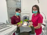 Dwie dentystki w maseczkach i rękawiczkach z uśmiechniętym pacjentem w gabinecie stomatologicznym.