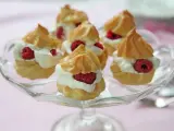 Små petit choux fyllda med grädde och hallon på ett glasfat.