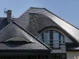 Dachówka karpiówka w koronkę pokrywa dach domu z kamiennym kominem i łukowym oknem.