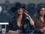 Mujer con sombrero tejano y chaqueta de cuero, disfrutando de un evento. Se aprecian otros tipos de tejanos en el público.