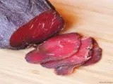 Bresaola co to? Ciemnoczerwone, cienko pokrojone plastry suszonej wołowiny na desce.
