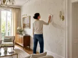 Une femme nettoie un mur avec un papier peint à motifs de feuilles. Elle utilise un chiffon pour peindre sur du papier peint, peut-être pour le rafraîchir.