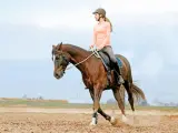 Reiterin auf braunem Pferd im Trab auf einem Sandplatz. Die Volten bedeuten für sie und ihr Pferd eine harmonische Lektion.
