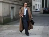 Mujer con abrigo largo marrón, traje de raya diplomática y corbata, luciendo un impecable tomboy style.