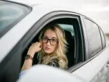 Blondynka w okularach siedzi za kierownicą białego samochodu. Pokazuje, jak nosić okulary, by wyglądać stylowo i pewnie.