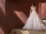 Suknia ślubna w kolorze rose ivory, z koronkowymi aplikacjami, na tle rustykalnej ściany.