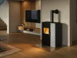 Estufa mixta pellets y leña canalizable, con fuego encendido, en un salón moderno con escaleras y TV.