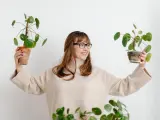 Mujer sonriente con gafas sostiene dos plantas altas de interior.