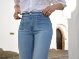 Mujer con vaqueros de tiro alto y camisa blanca, ajustándose la cintura.