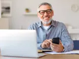 Uśmiechnięty senior z laptopem i telefonem, korzystający z ulgi dla seniora w PIT-37.