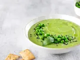 Cremoso hummus di piselli guarnito con piselli freschi, basilico e semi di sesamo, servito con cracker croccanti.