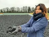Une femme tient dans ses mains un échantillon de fibre, un avis carrière en fibre. L'arrière-plan montre une carrière équestre.