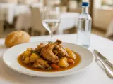 Conejo guisado con patatas y zanahorias en un plato blanco, acompañado de pan y agua.