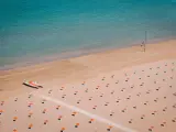 Pusta plaża w Rimini z rzędami pomarańczowych parasoli i łodzią ratowniczą.