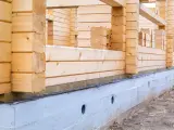 Budowa domu z bali. Widoczna izolacja drewna od betonu, chroniąca przed wilgocią.