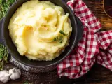 Una ciotola di cremoso purè di patate, guarnito con timo fresco, accanto ad aglio e un tovagliolo a quadri rossi.