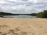Piaskowa plaża nad jeziorem, z pomostami i łódkami. W oddali las, chmury na niebie. Idealne miejsce na wypoczynek nad wodą.