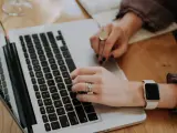 Dłonie piszące na klawiaturze laptopa, z widocznym zegarkiem i pierścionkami.