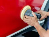Ręce polerują czerwony lakier auta maszyną polerską. To kluczowy etap, jak woskować auto, by uzyskać lustrzany połysk i ochronę.