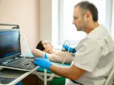 Lekarz wykonuje badanie USG piersi. Pacjentka leży na kozetce, a lekarz w rękawiczkach przykłada głowicę aparatu. Badanie jest ważne dla kobiet, które przeszły mastektomię, pomagając w diagnostyce i monitorowaniu stanu zdrowia, co może wpływać na ich g...