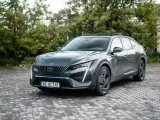 Nowoczesny Peugeot 408 Hybrid w ciemnoszarym kolorze, zaparkowany na brukowanym podjeździe, otoczony zielenią.
