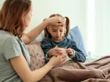 Mutter prüft Fieber bei krankem Kind im Bett. Die Krankschreibung für die Schule ist nötig, damit das Kind sich erholen kann.