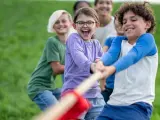 Des enfants joyeux jouent à la corde dans un champ d'herbe verte.