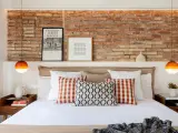 Ideas para decorar la pared de la cabecera de la cama: ladrillo visto, cuadros y lámparas naranjas.