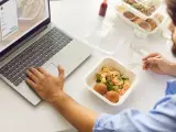 Mężczyzna pracuje przy laptopie i je dietetyczny posiłek z pudełka.