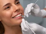 Uśmiechnięta kobieta podczas badania stomatologicznego. Dentysta sprawdza zęby, by upewnić się, że bonding nie niszczy zębów.