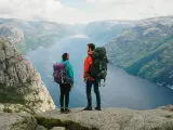 Två vandrare med stora ryggsäckar står på en klippa och blickar ut över en fjord i Norge. Perfekt för camping i Norge.