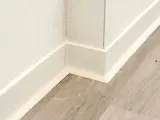 Angolo di una stanza con parquet grigio e battiscopa bianco appena installato.