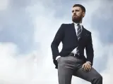 Elegancki mężczyzna w granatowej marynarce i szarych spodniach, z ręką w kieszeni, patrzy w dal. Stylowe granatowa marynarka stylizacje.